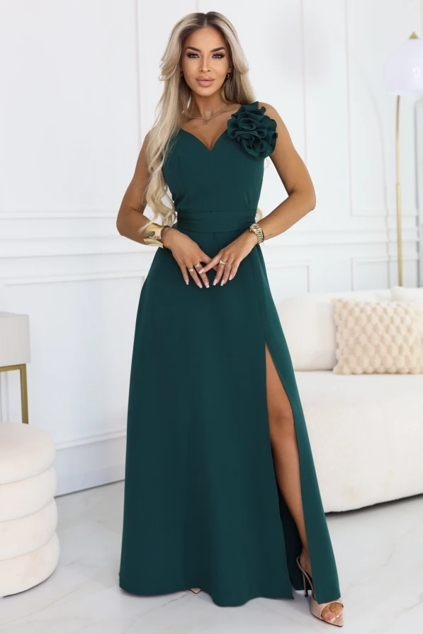 Modelka prezentuje elegancką butelkowozieloną suknię maxi na jedno ramię z ozdobnym kwiatem 3D i wysokim rozcięciem na nodze.