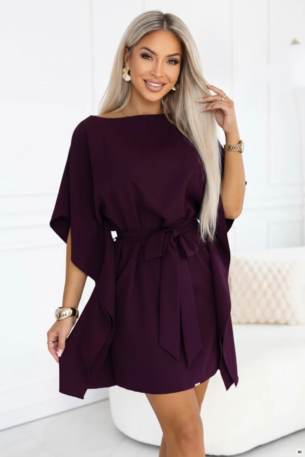 Modelka w sukience kimono marki Numoco w kolorze dojrzałej śliwki, z dekoltem w łódkę, szerokimi rękawami, paskiem wiązanym w talii i drapowanymi bokami, o długości przed kolano.
