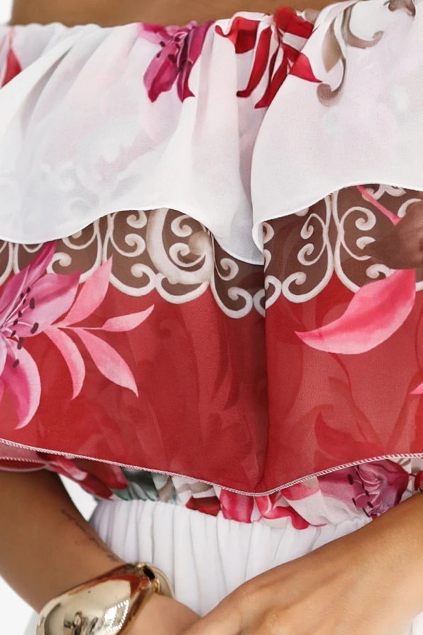 Modelka z gracją prezentuje letnią sukienkę maxi hiszpankę z falbaną i kwiatowym wzorem w odcieniach czerwieni i różu. Jej swobodna poza i uśmiech podkreślają romantyczny, kobiecy charakter tej stylizacji od Numoco Basic.