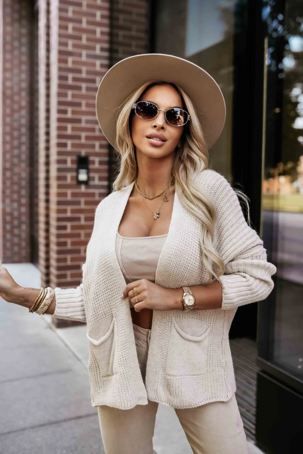 Kobieta w stylowej beżowej narzutce z kieszeniami pozuje na tle miejskiej zabudowy.